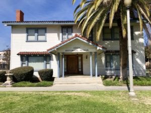 Front facing view of Azusa Historical Museum, which is an old house with a large palm tree in front of it.