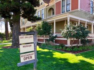 Historic colonial style home with large trees and sign displaying Art Gallery, Museum and Restaurant Open